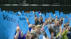 Delegates at national delegate conference raise blue voting cards above their heads